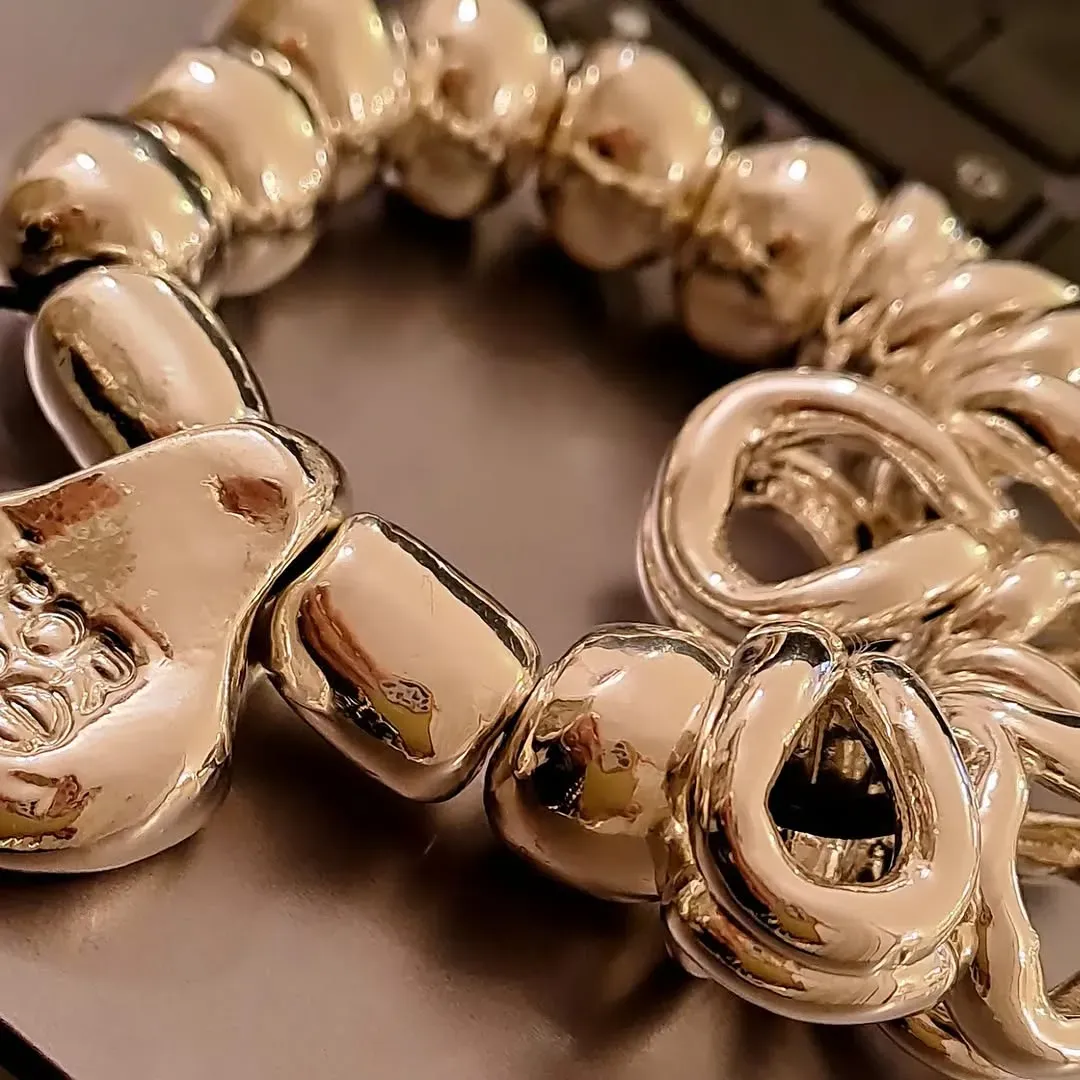 Braccialetto di perline d'argento appoggiato su una superficie scura, che riflette la luce.