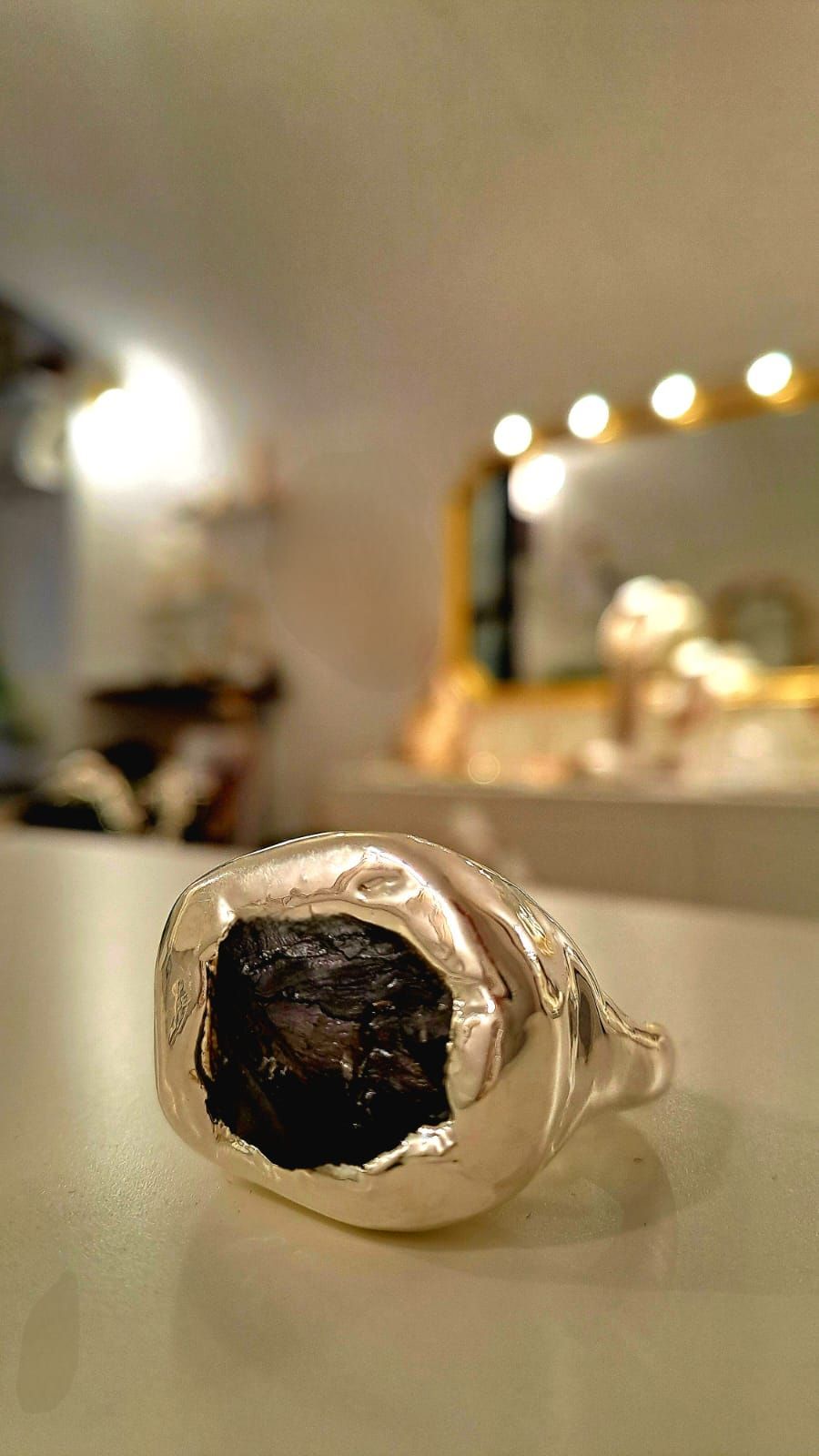 Un anello d'argento è appoggiato su un tavolo bianco davanti a uno specchio.