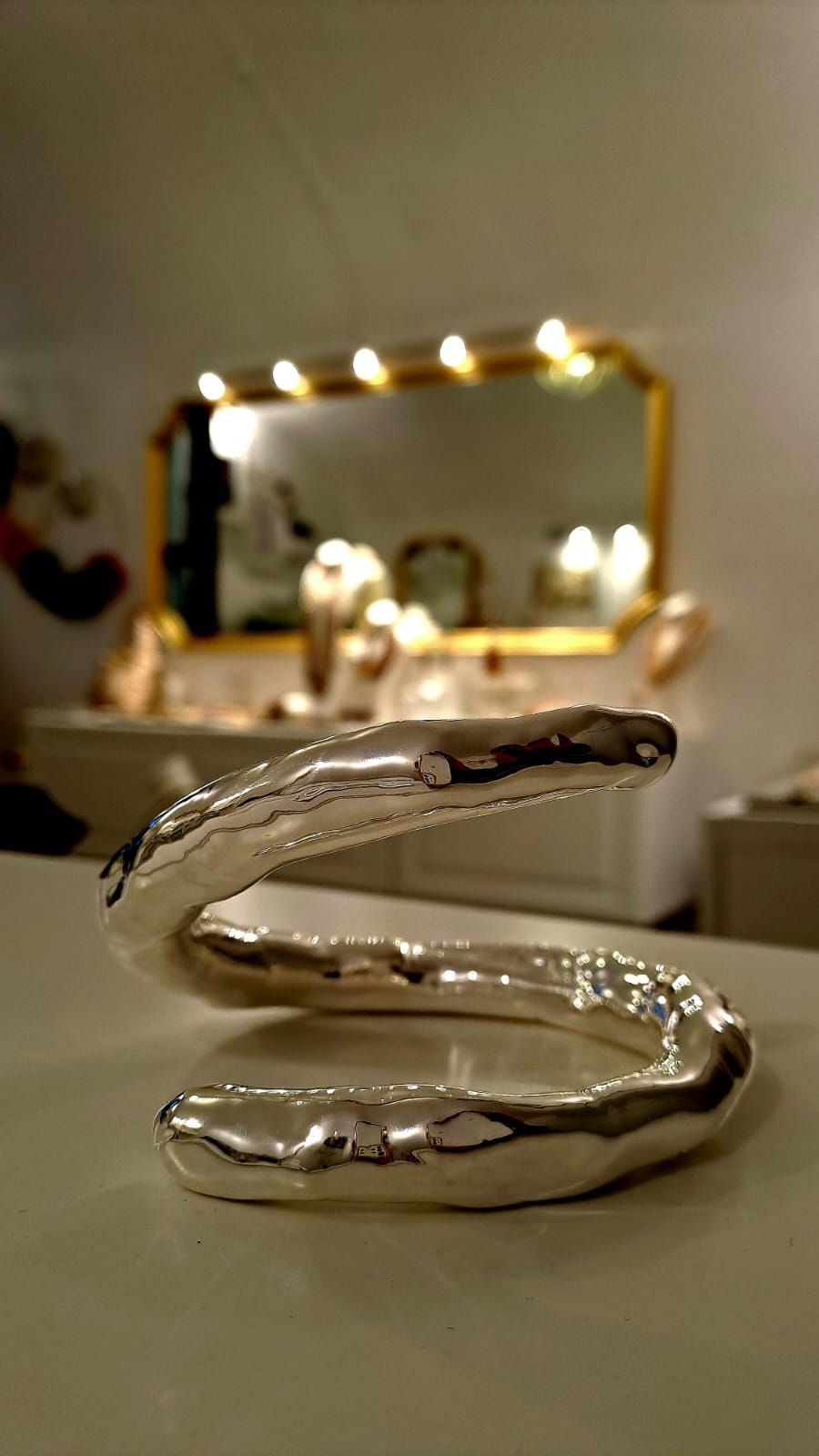 Un oggetto d'argento è appoggiato su un tavolo davanti a uno specchio.