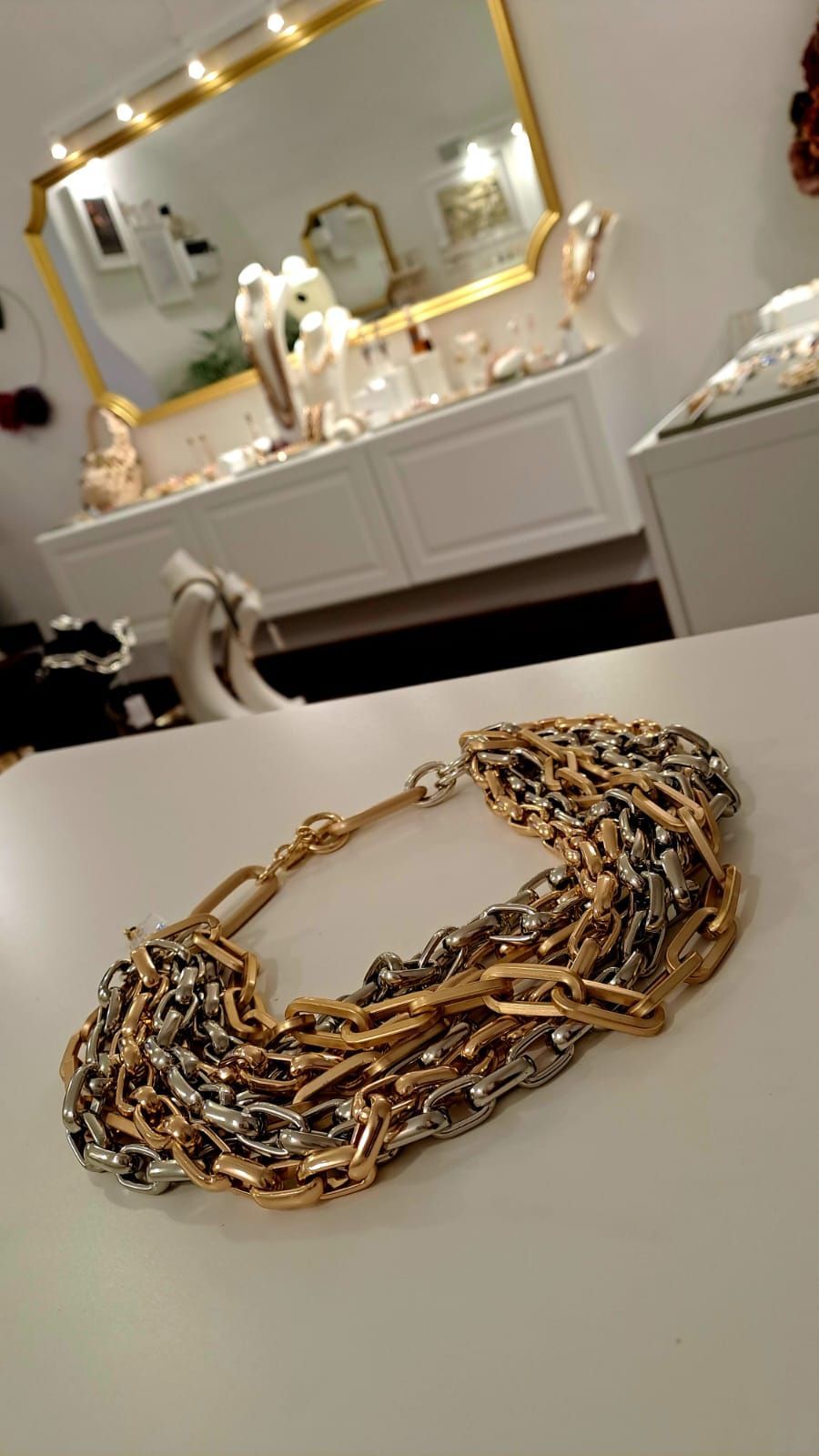 Una collana d'oro e d'argento è appoggiata su un tavolo davanti a uno specchio.