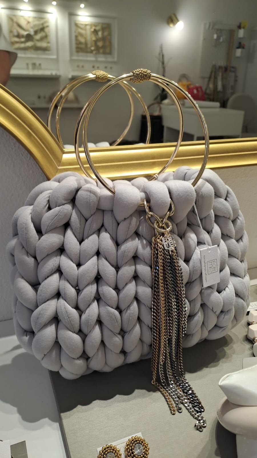 Una borsa grigia lavorata a maglia con manici dorati è appoggiata su un tavolo davanti a uno specchio.