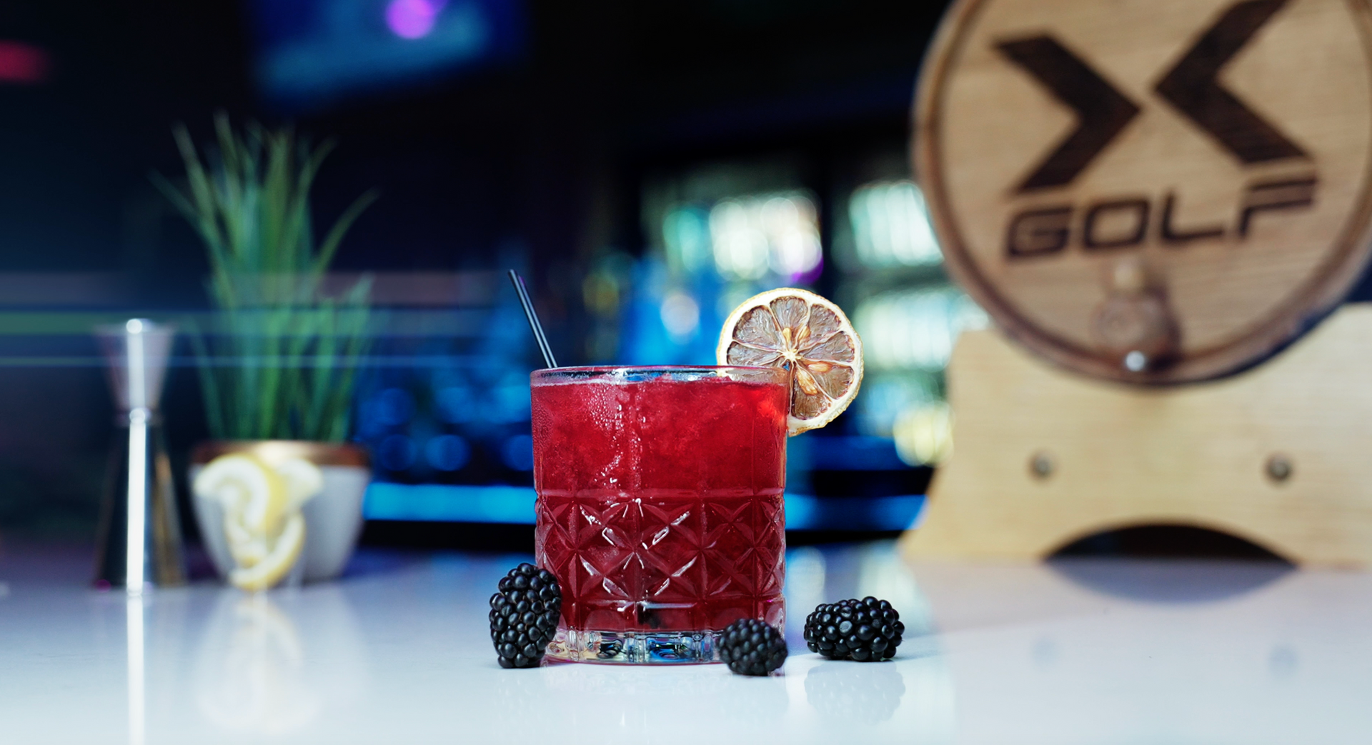 A glass of red liquid with blackberries and a lemon slice on a table.