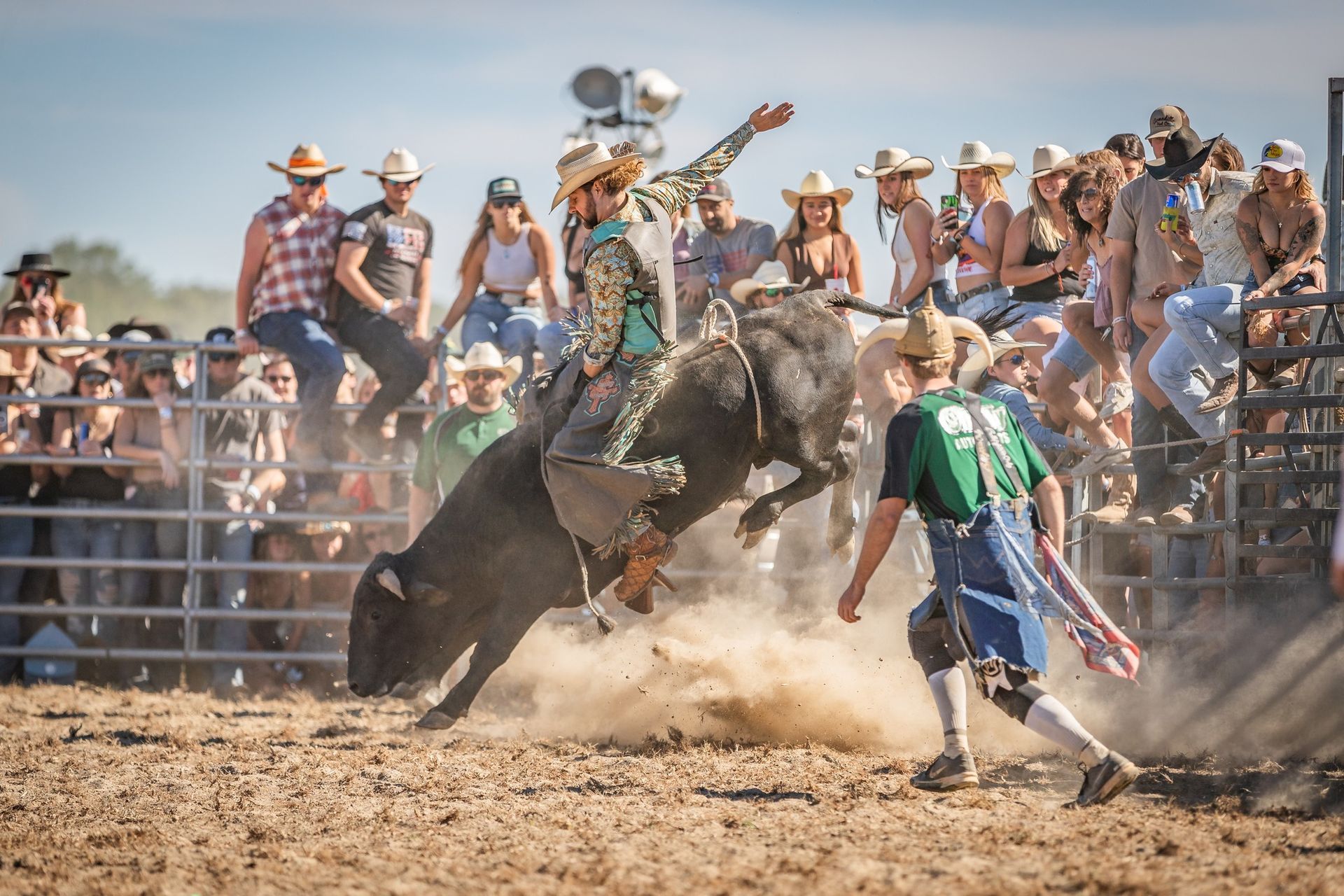 Bull rider on a bucking bull at a rodeo, crowd watches, dirt flying.