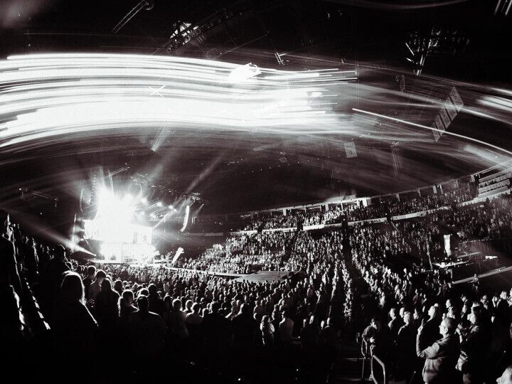 Concert at a stadium. Black and white. Large crowd watching stage with bright lights and streaks of light.
