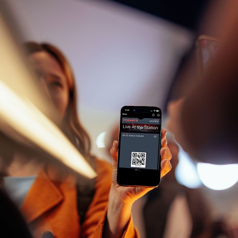 A woman is holding a cell phone that says live at the station