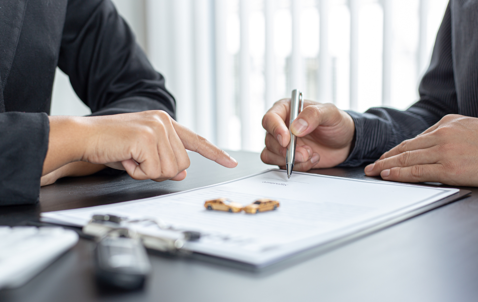 Two people in business attire sign a document on a desk, with one person pointing and the other holding a pen.