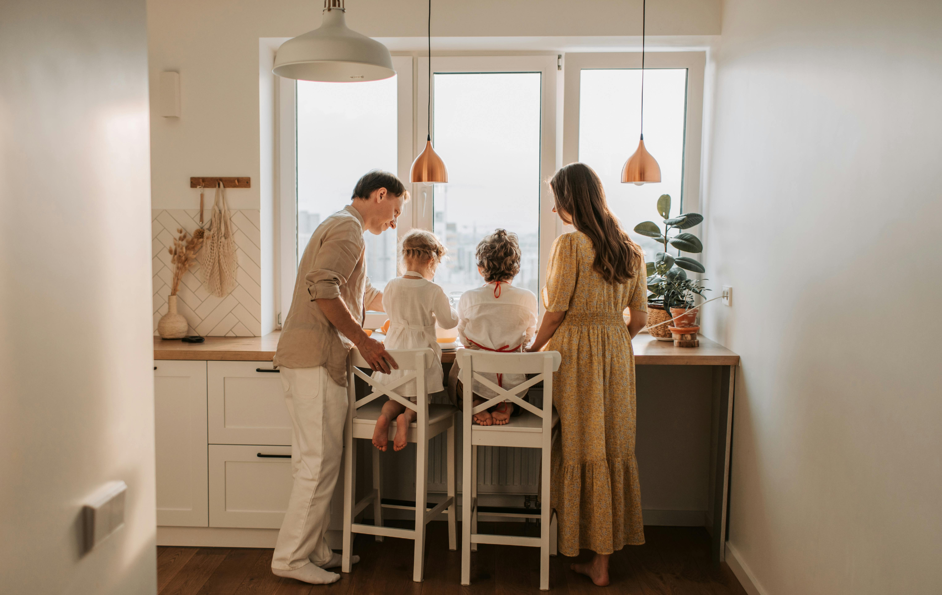 A family standing together in a kitchen, looking out a large window toward the light.
