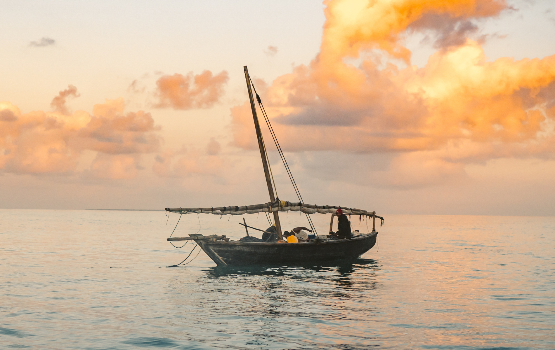 A small wooden boat floats on calm water under a golden, cloudy sunset sky.