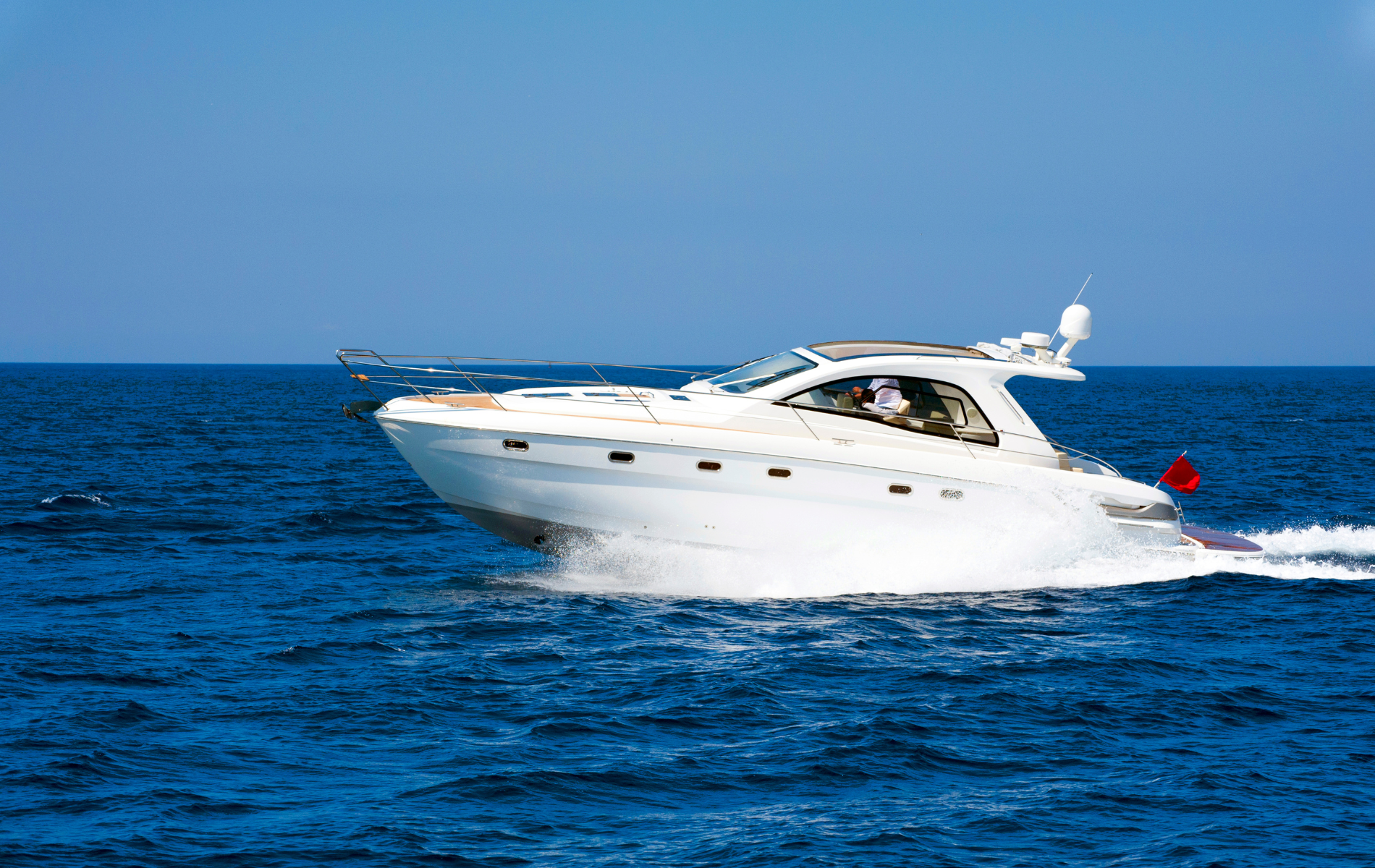 A white motor yacht cruising across the open blue ocean, leaving a white wake behind it.