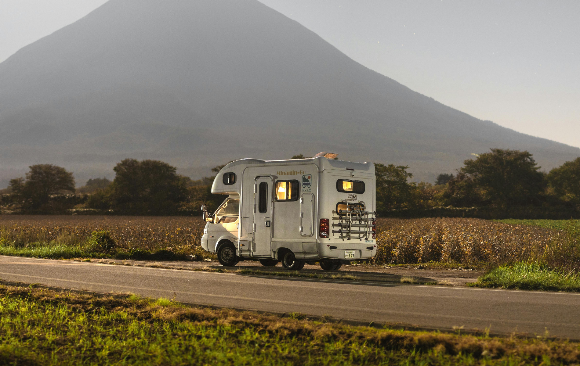 A white camper van parked on the side of a road in a field with a large mountain in the background.