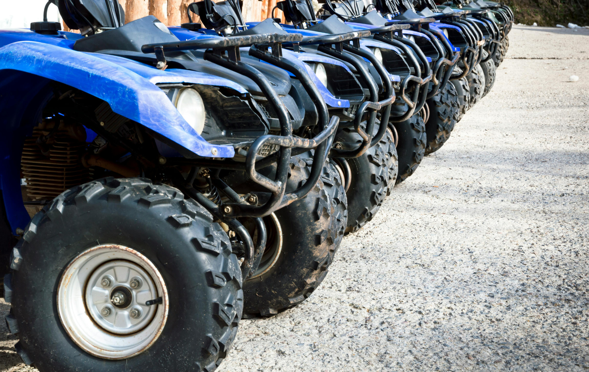 A line of blue all-terrain vehicles (ATVs) parked in a row on a gravel surface.