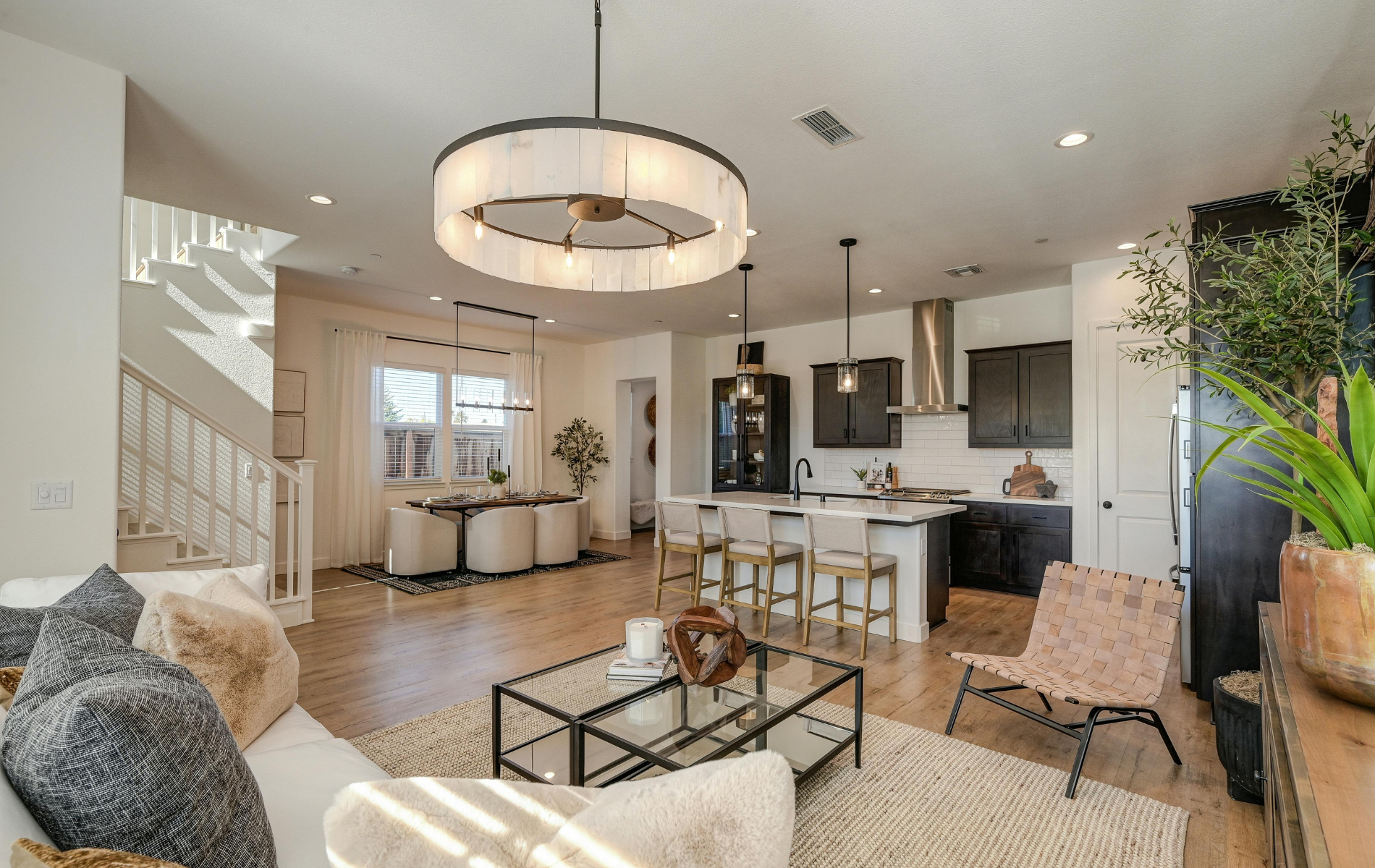 Open-concept living room with a neutral sofa, glass coffee table, kitchen island with bar stools, and dining area.