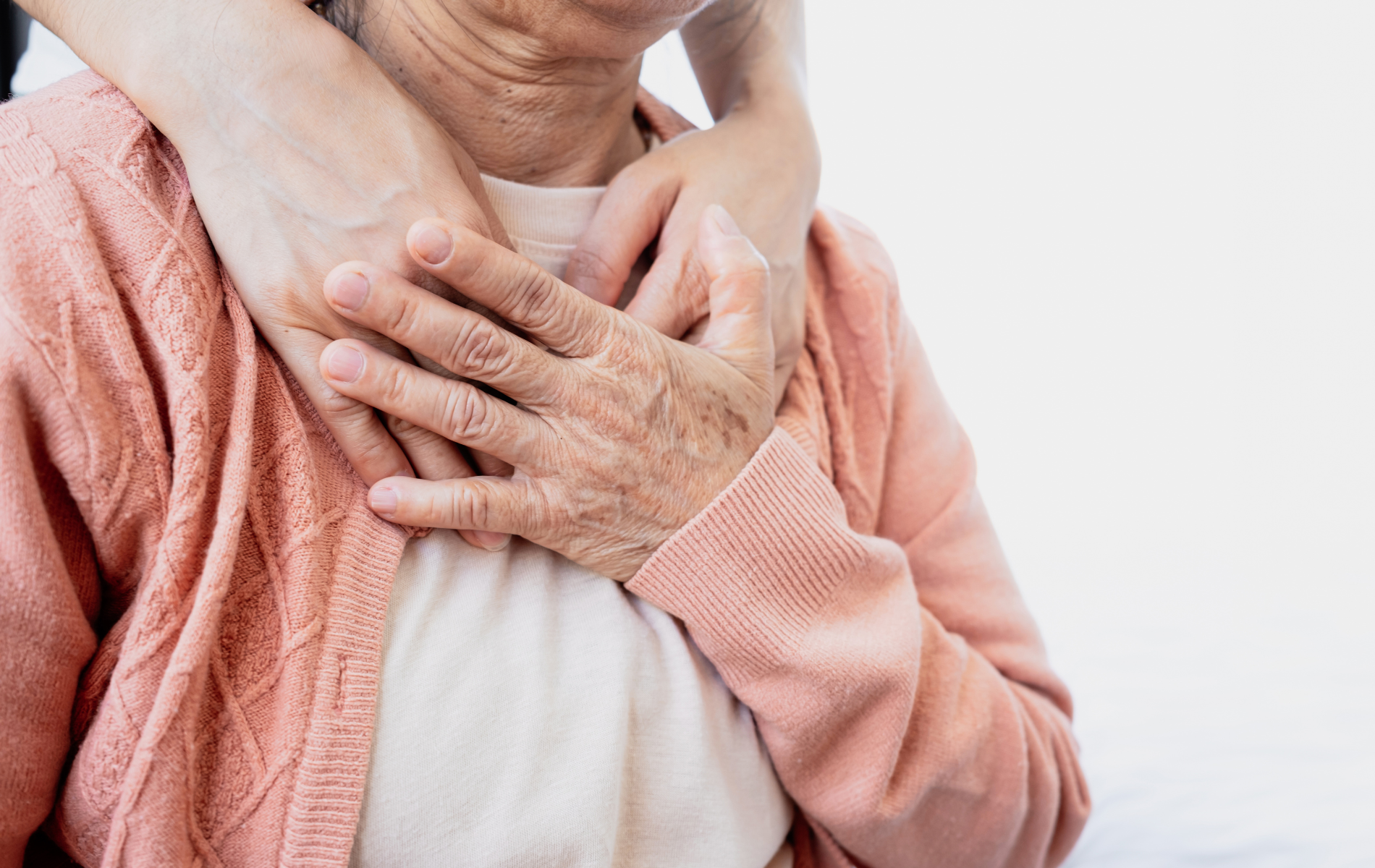 A person with their hands gently resting on an older person's chest and shoulders in a comforting gesture.