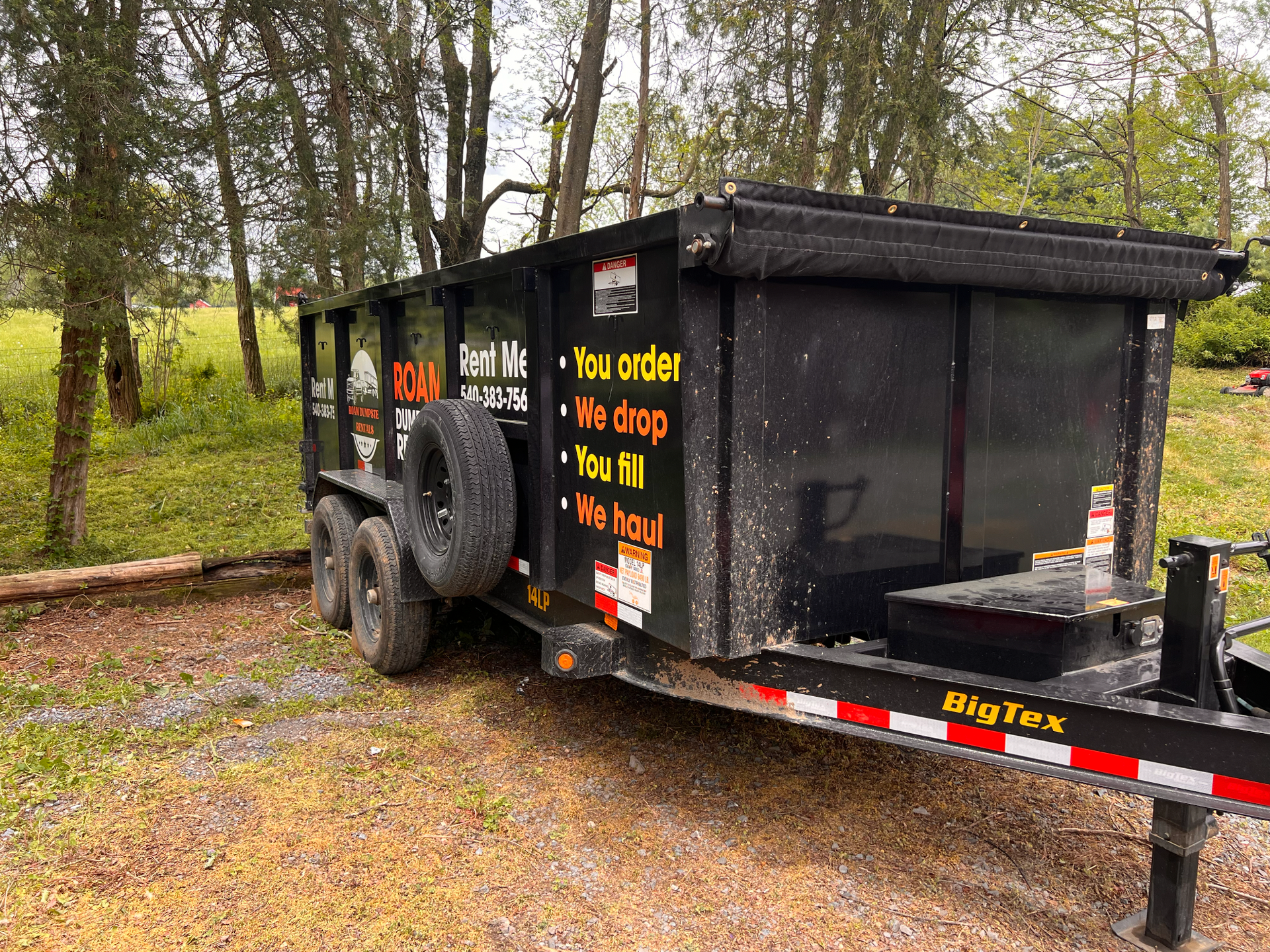 A large white dumpster is parked in front of a brick house.