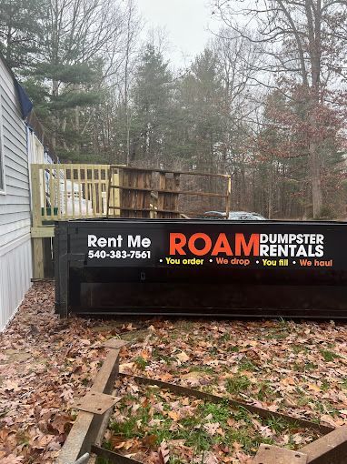 A dumpster with a sign that says `` rent me roam dumpster rentals '' is sitting in front of a house.