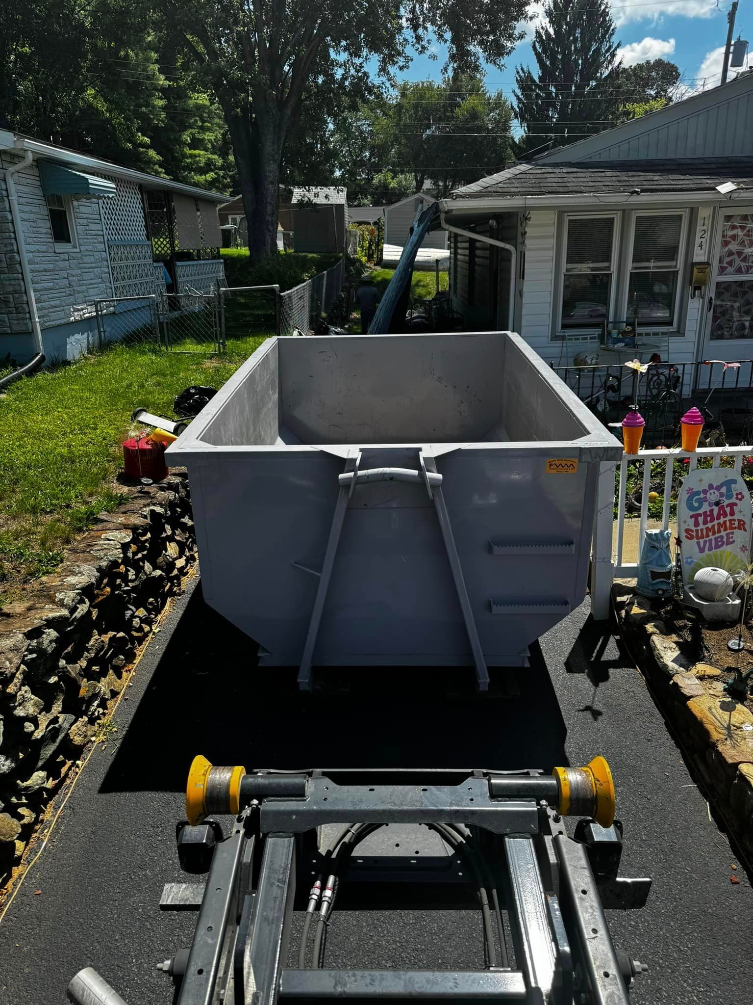 A large dumpster is sitting on the side of the road next to a house.