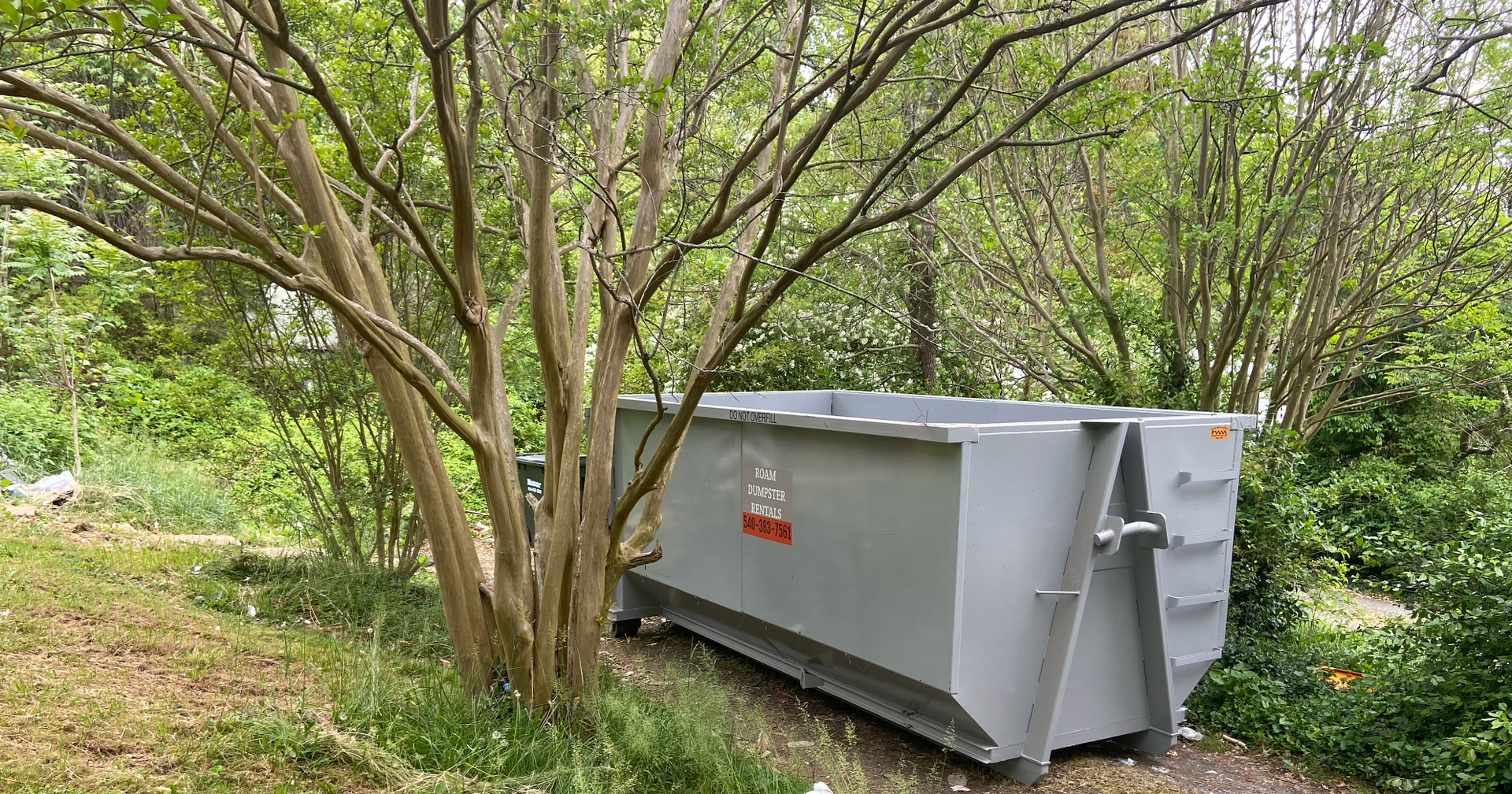 A dumpster on a trailer is parked in front of a garage.