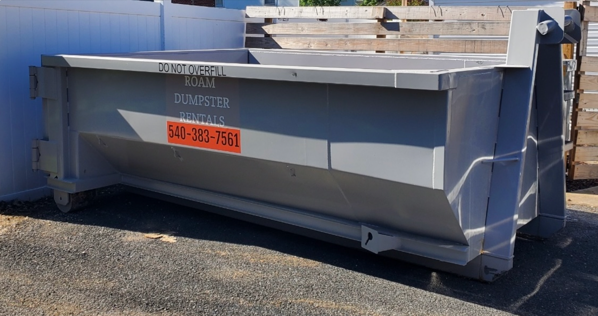 A dumpster on a trailer is parked in front of a garage.