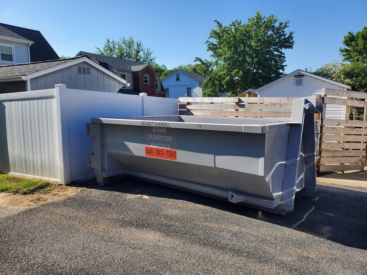 A large concrete dumpster is parked in a driveway next to a white fence.