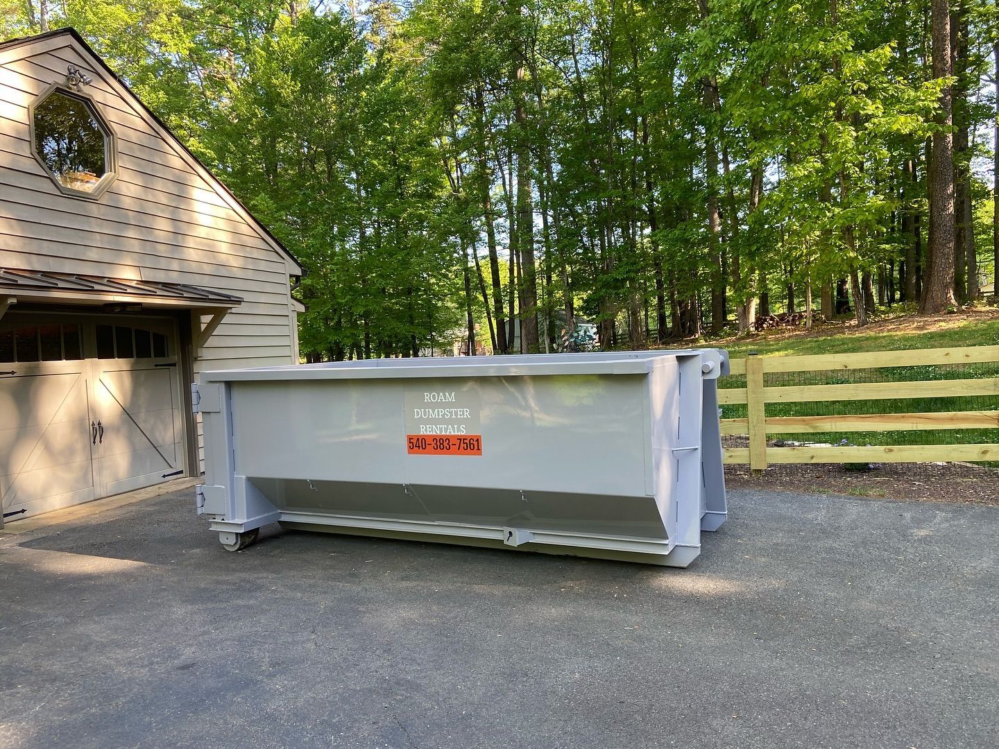 A large dumpster is parked in a driveway in front of a house.