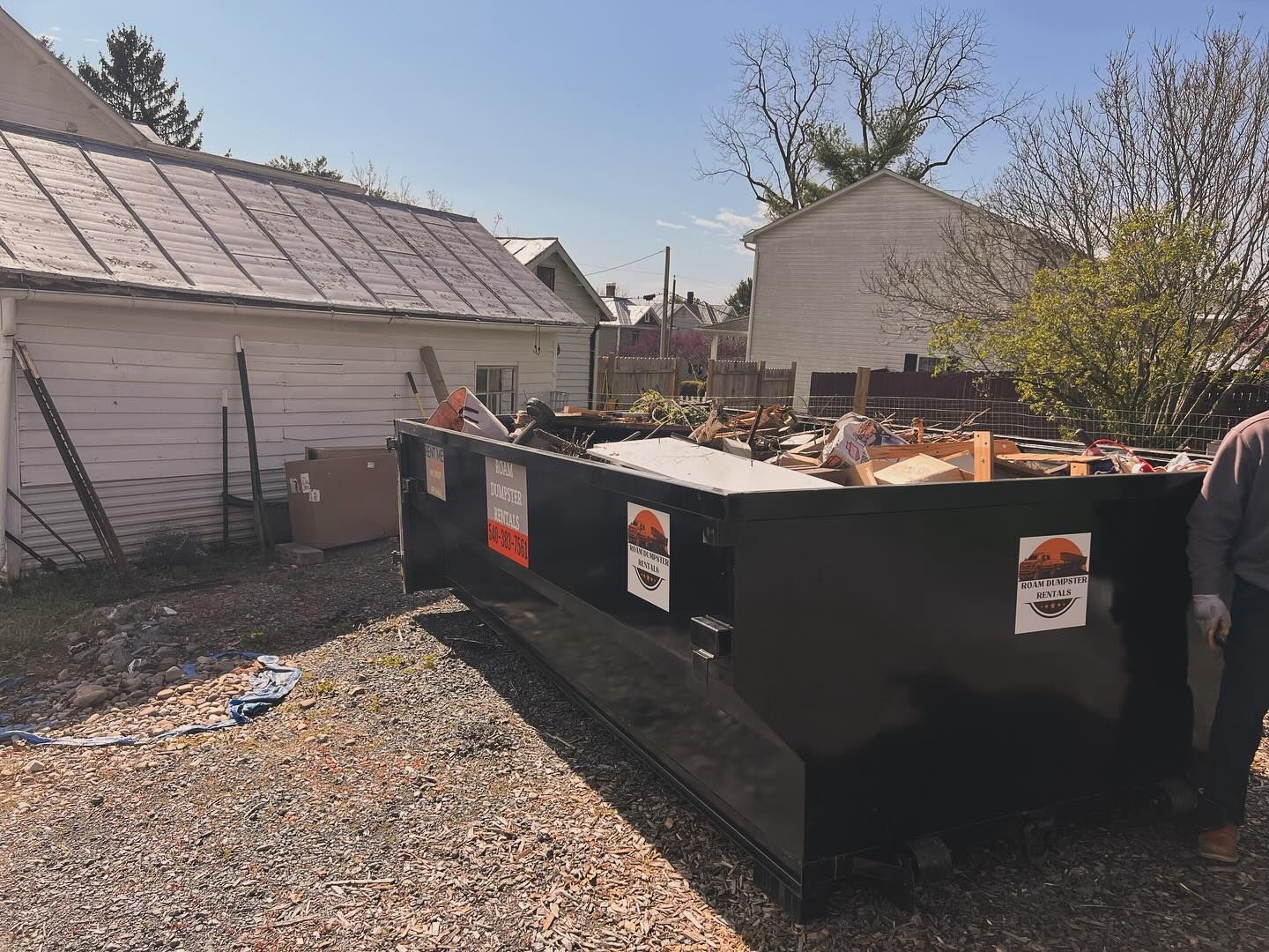 A man is standing next to a dumpster in a driveway.