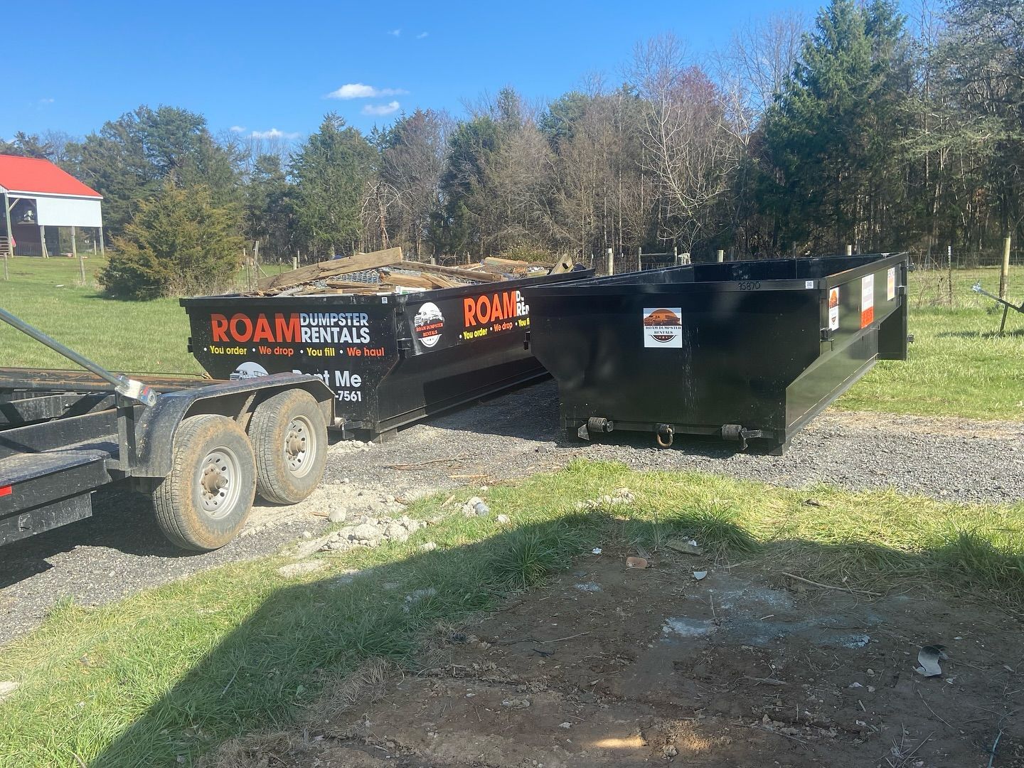 A dumpster is being pulled by a trailer in a field.