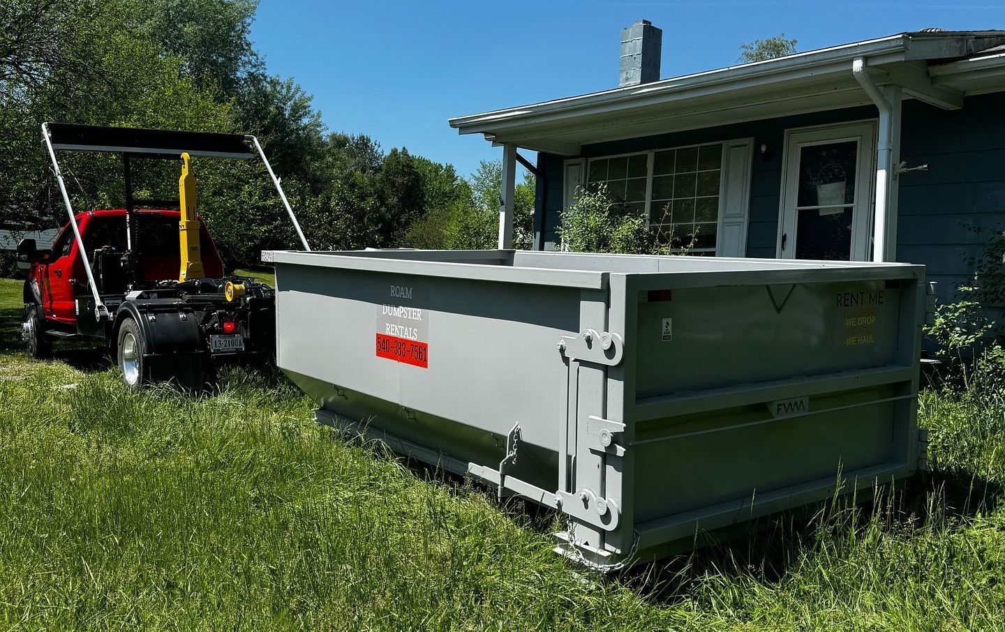 A dumpster on a trailer is parked in front of a garage.