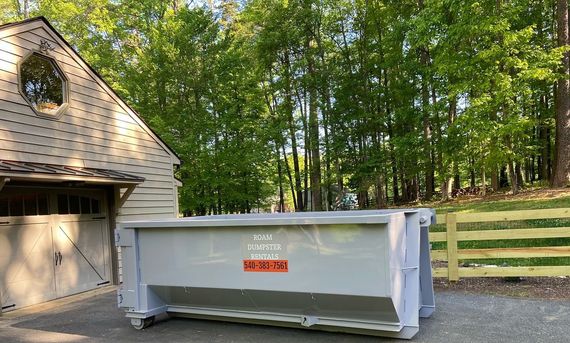 A large dumpster is parked in front of a garage.