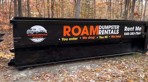 A dumpster from roam dumpster rentals is sitting in the woods in Harrisonburg, Virginia. 