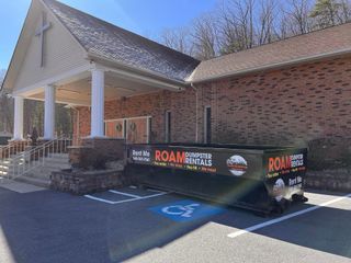 A Roam dumpster rental is parked in front of the Lighthouse Gospel Tabernacle Church in Elkton, Virginia.