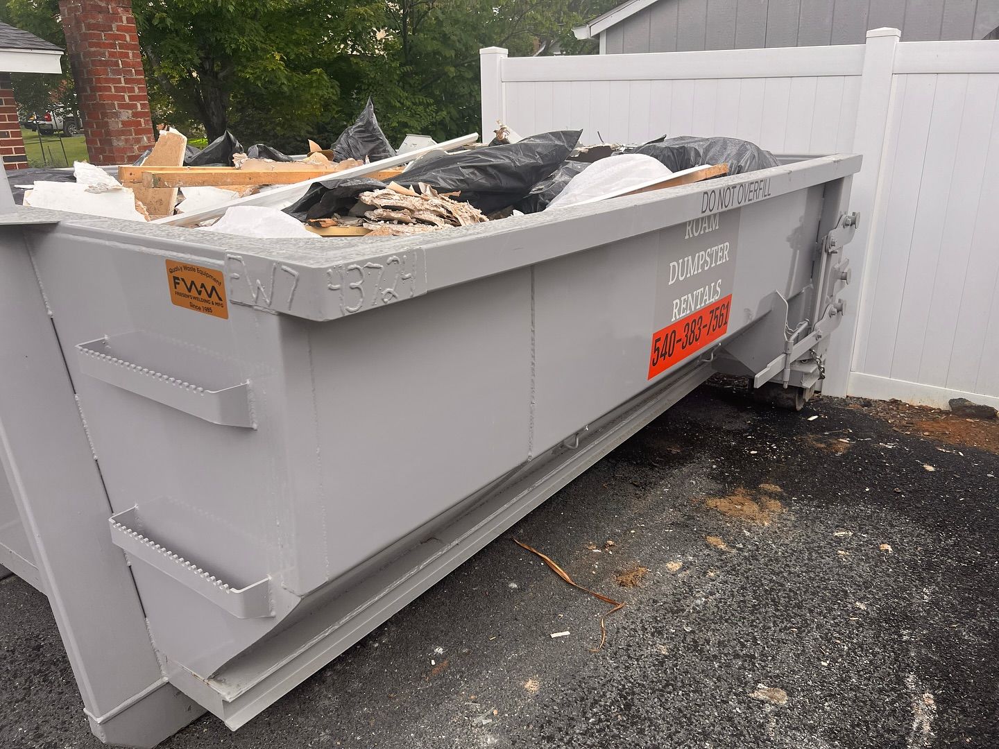 A dumpster on a trailer is parked in front of a garage.