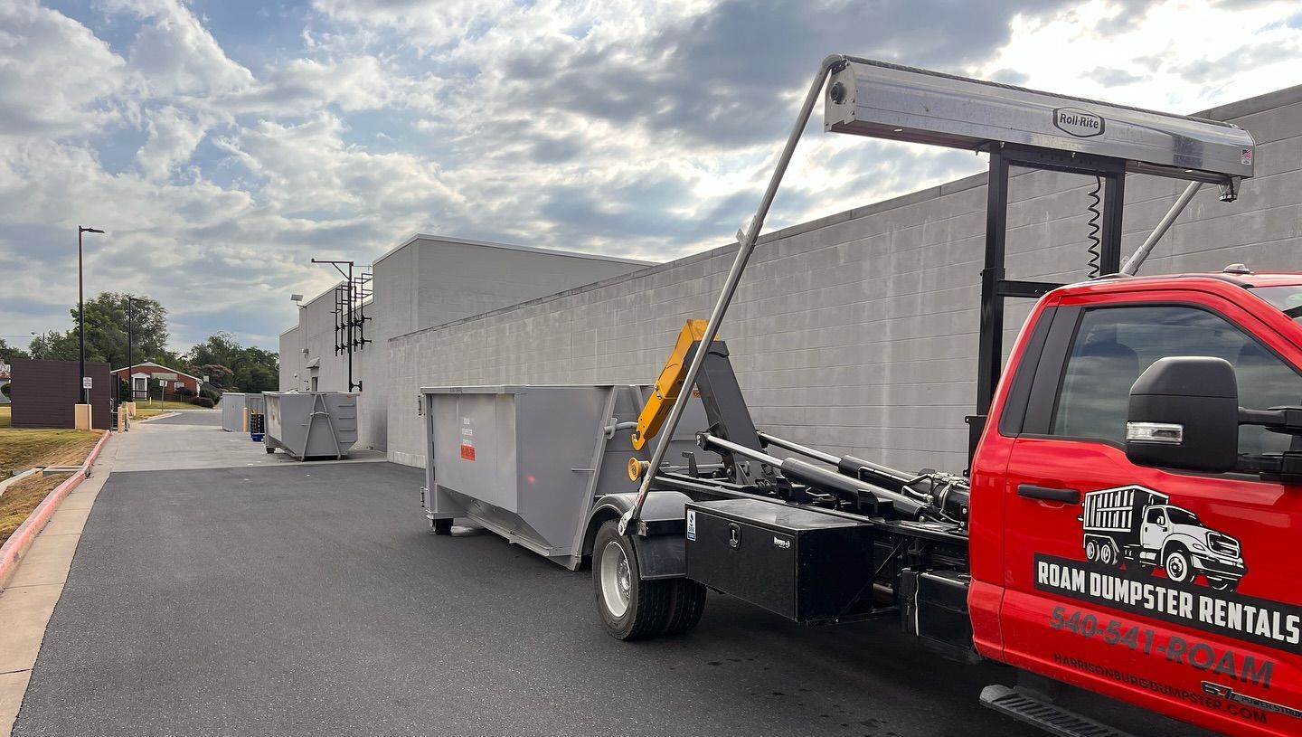 A red dump truck is pulling a dumpster in front of a building.