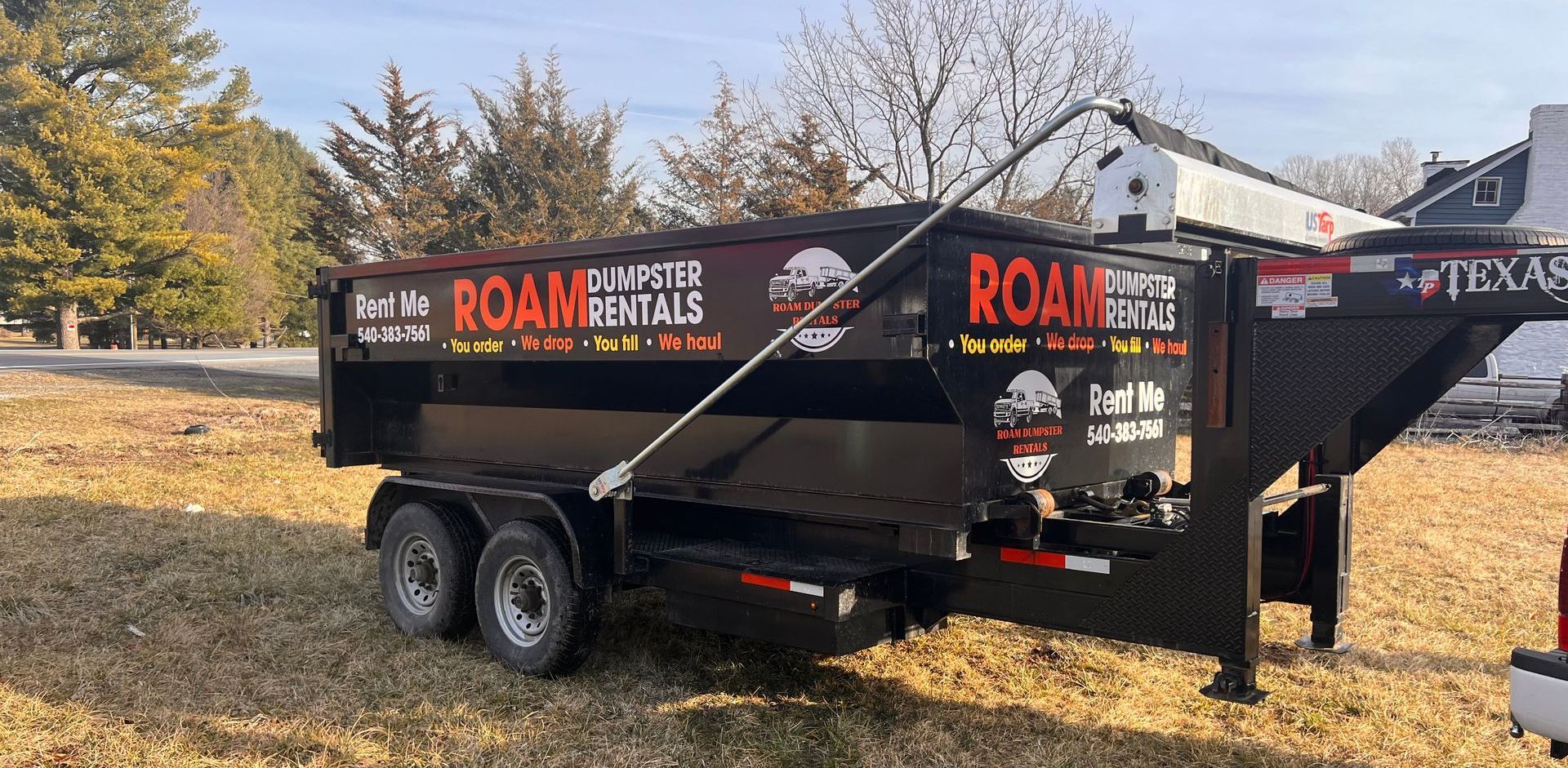 A dumpster trailer is parked in a field next to a truck.