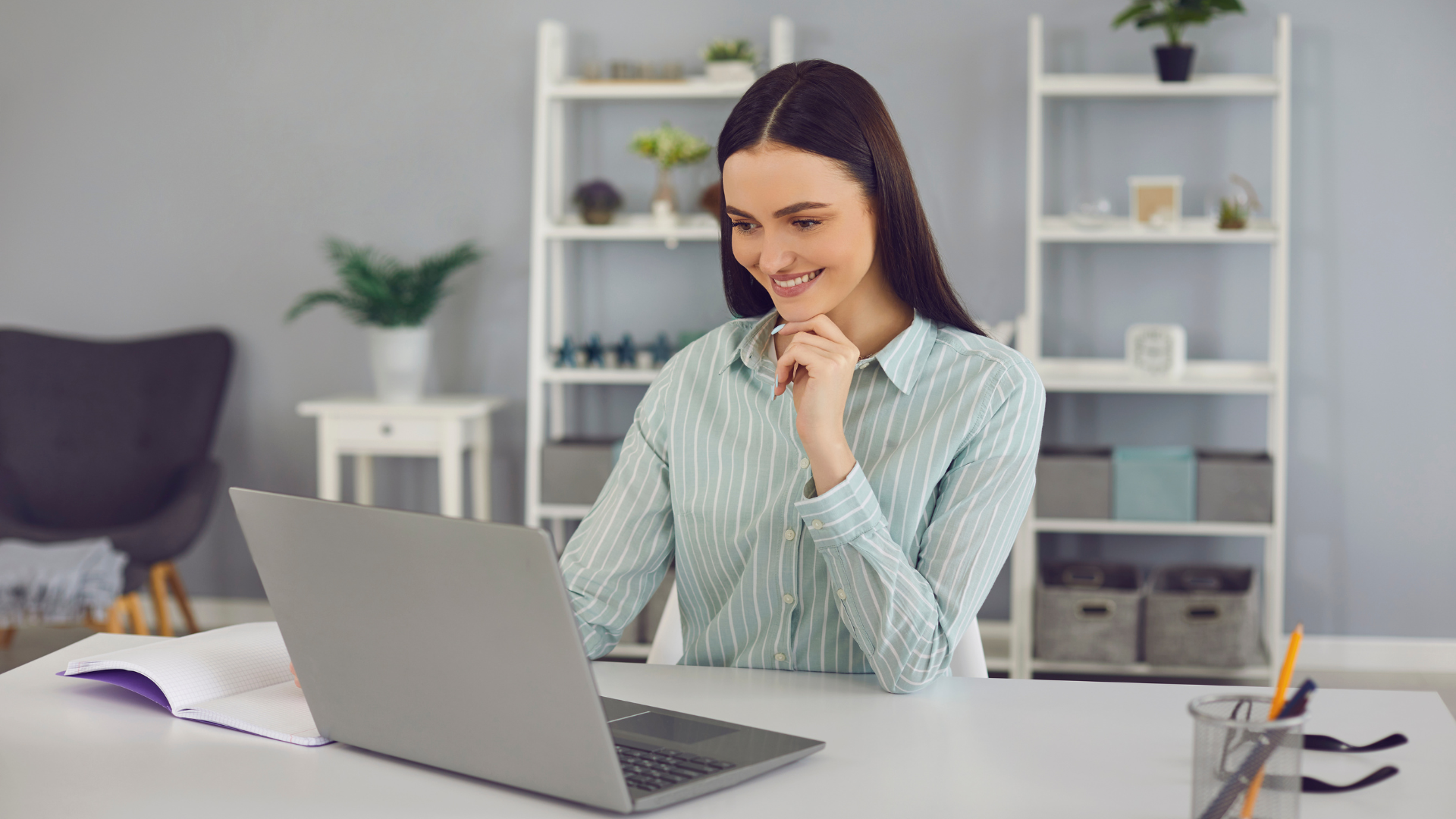 A woman is sitting at a desk using a laptop computer.