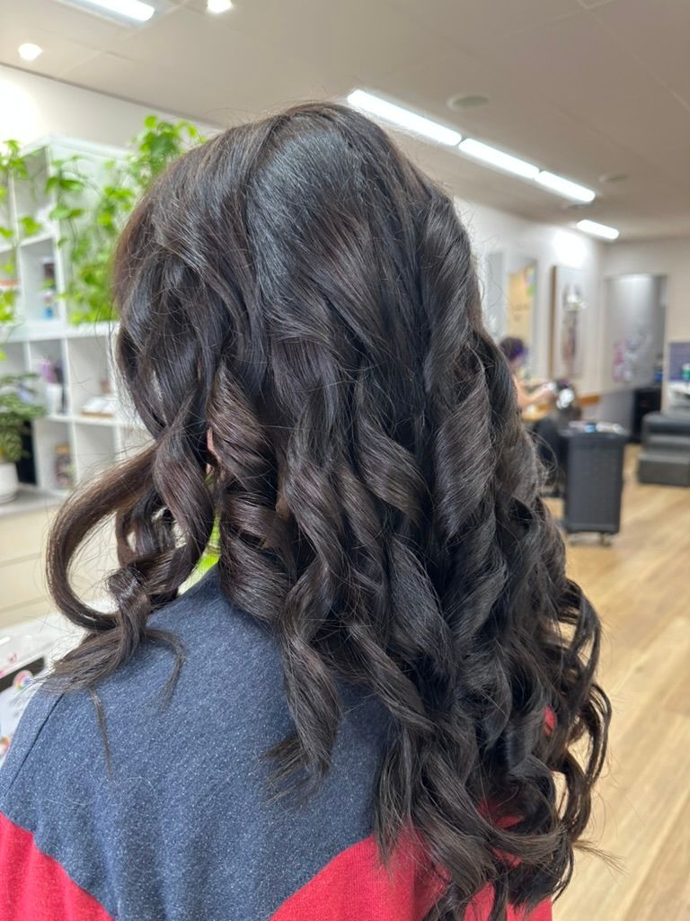 Back view of a person with long, dark, curled hair in a salon chair