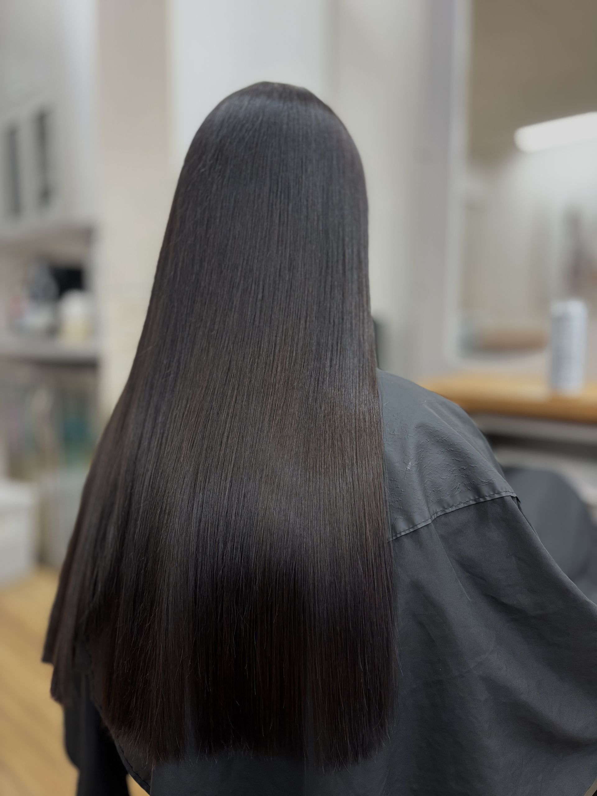 Person with long straight black hair seen from behind in a blurred indoor setting