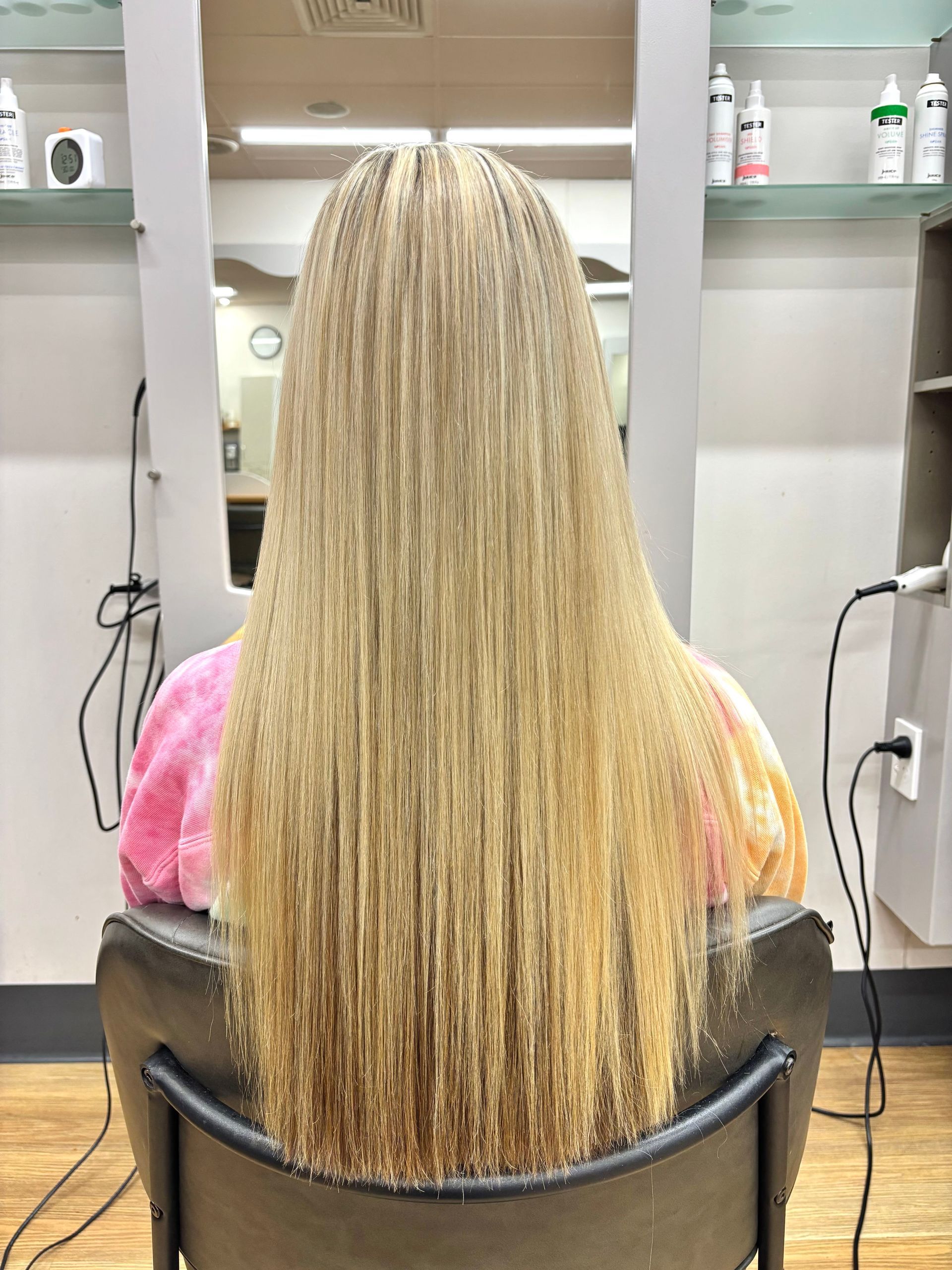 Hair stylist working on a seated client in a salon with mirrors and warm lighting.