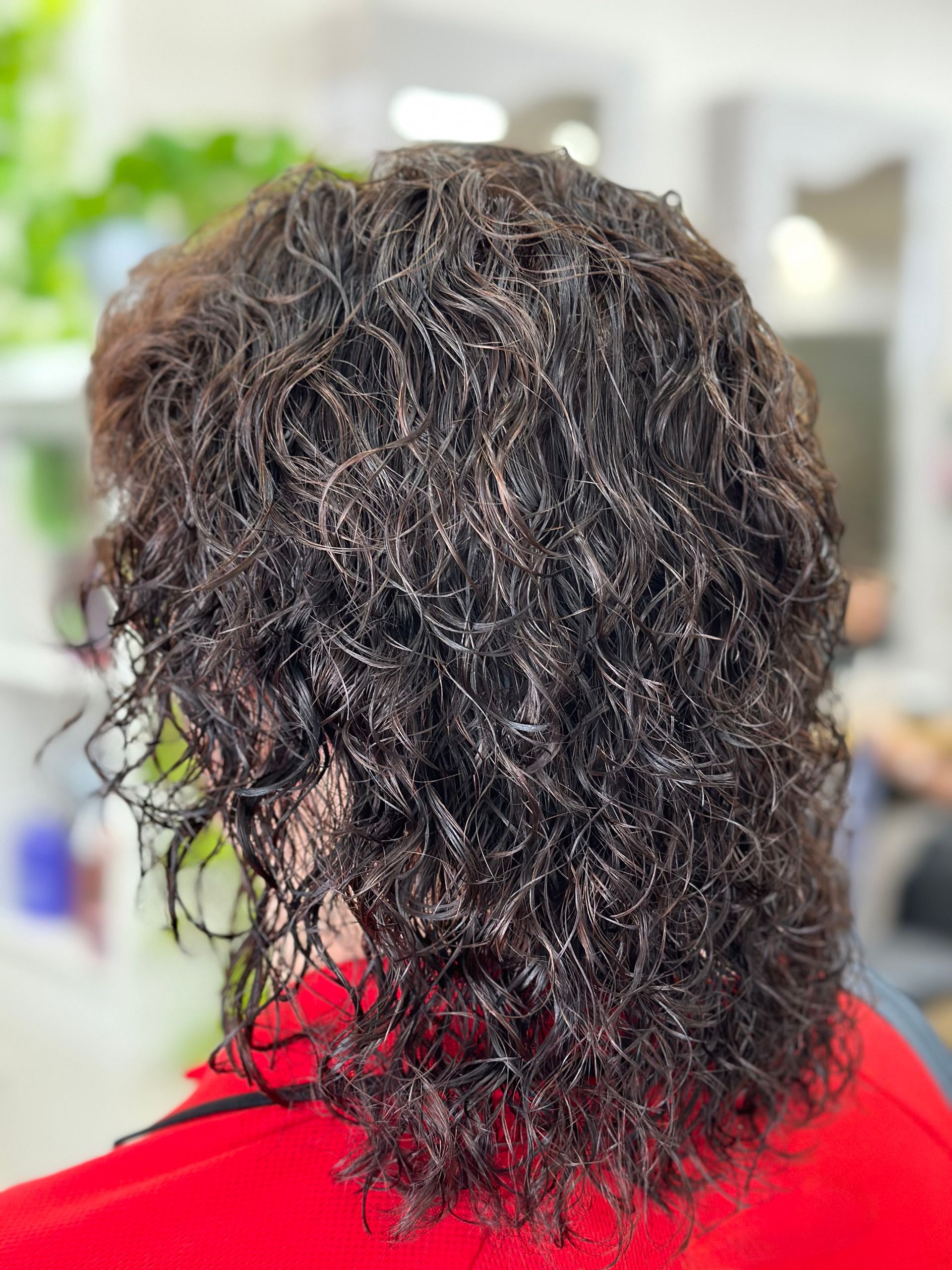 Back view of a person with curly dark hair wearing a red top in a bright indoor setting