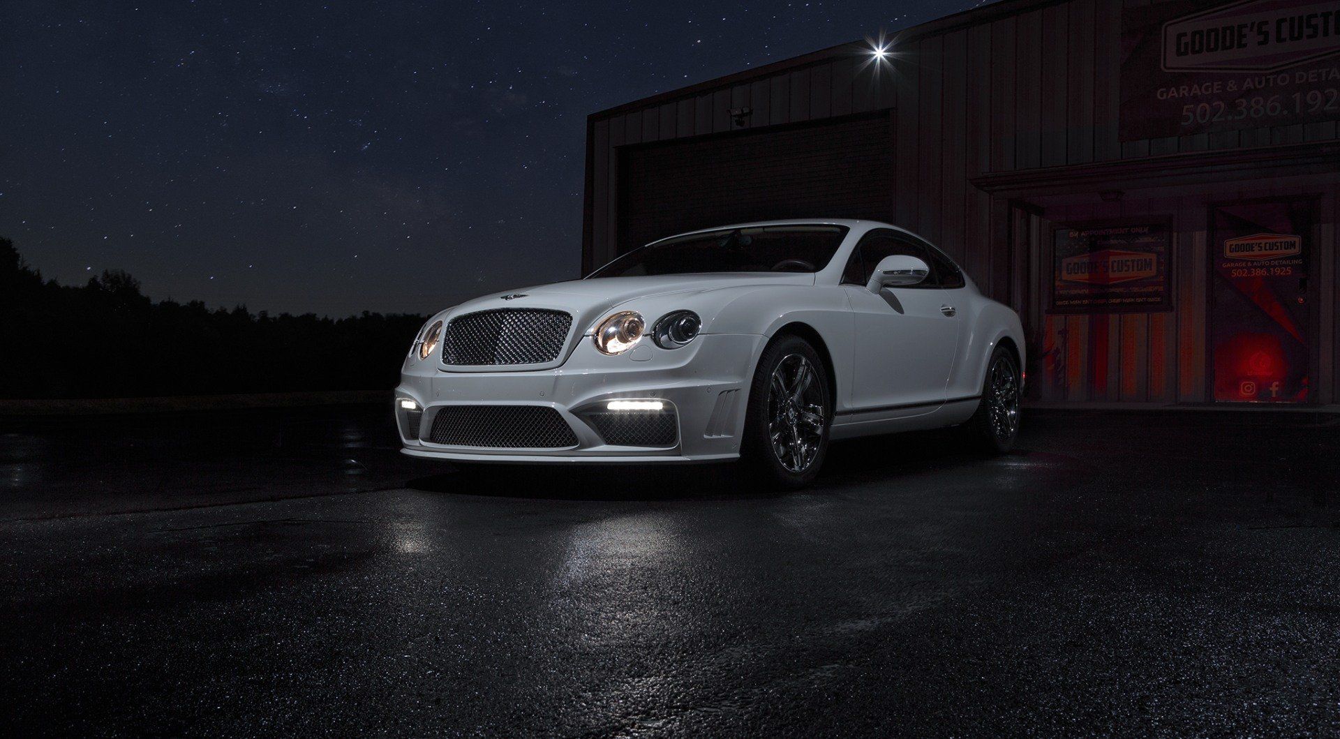 A white bentley continental gt is parked in front of a garage at night.