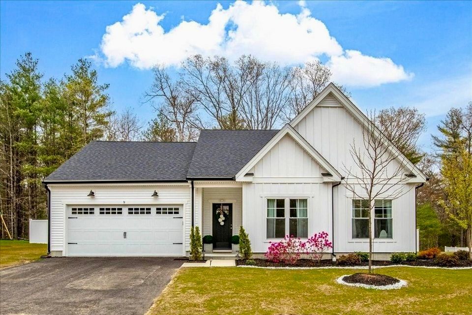 White farmhouse-style home with black roof and garage door, set on green lawn.