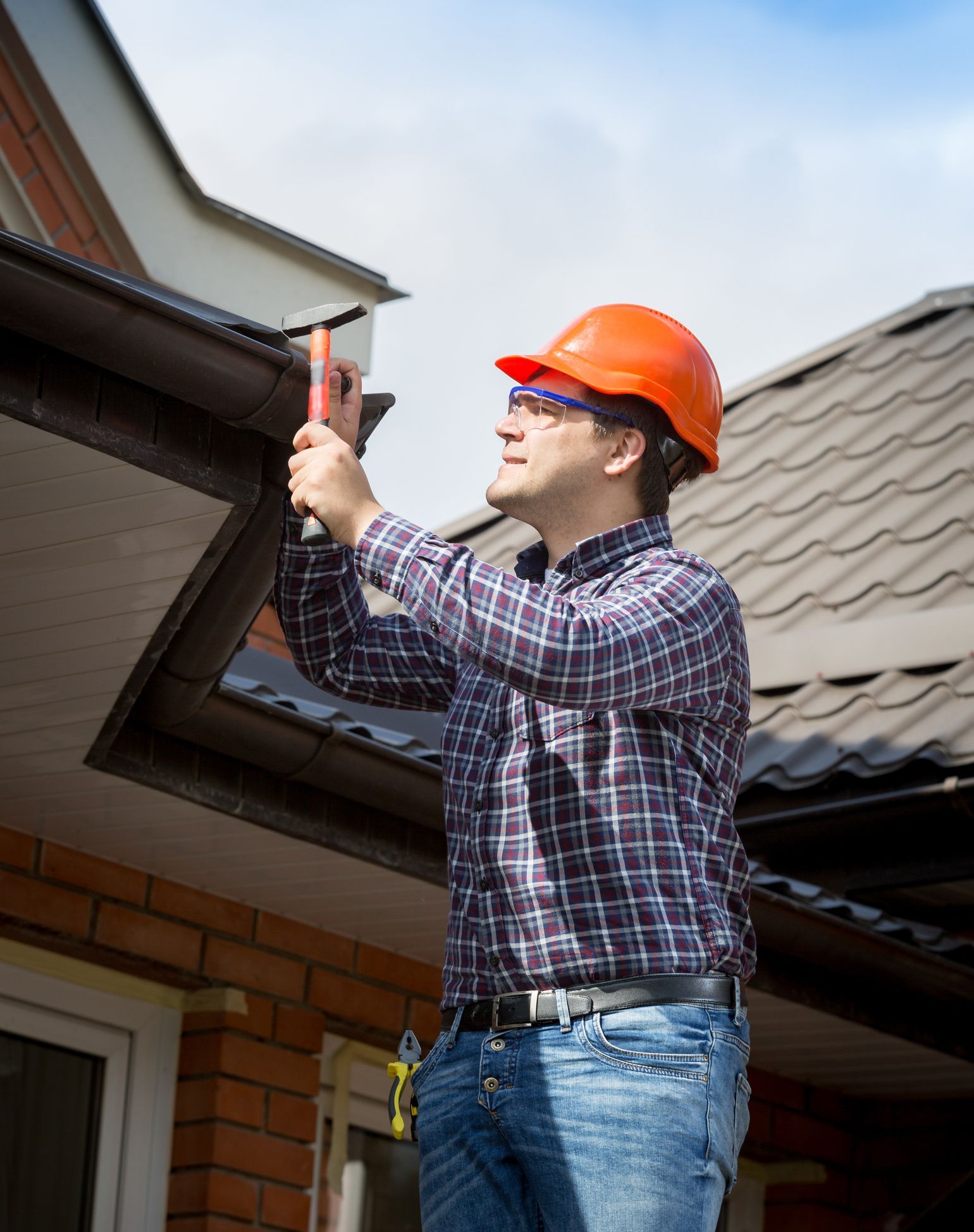 Young handyman with a safety hat uses a hammer and nail to fix a house’s roofing.