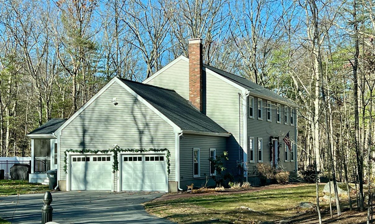 A large house with two garages is surrounded by trees on a sunny day.