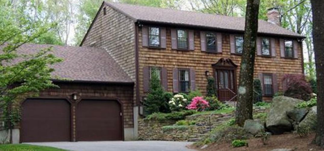 A large brick house with two garage doors is surrounded by trees.