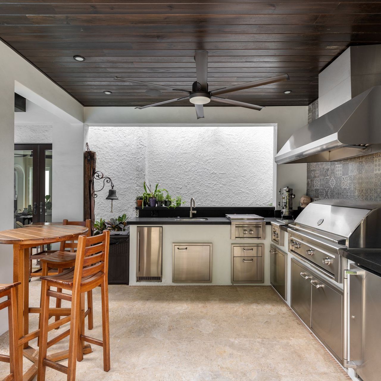 Modern outdoor kitchen and. luxury with grill, stove, extractor hood, wooden ceiling with fan, wooden tables and benches, chop tap, tiled wall.