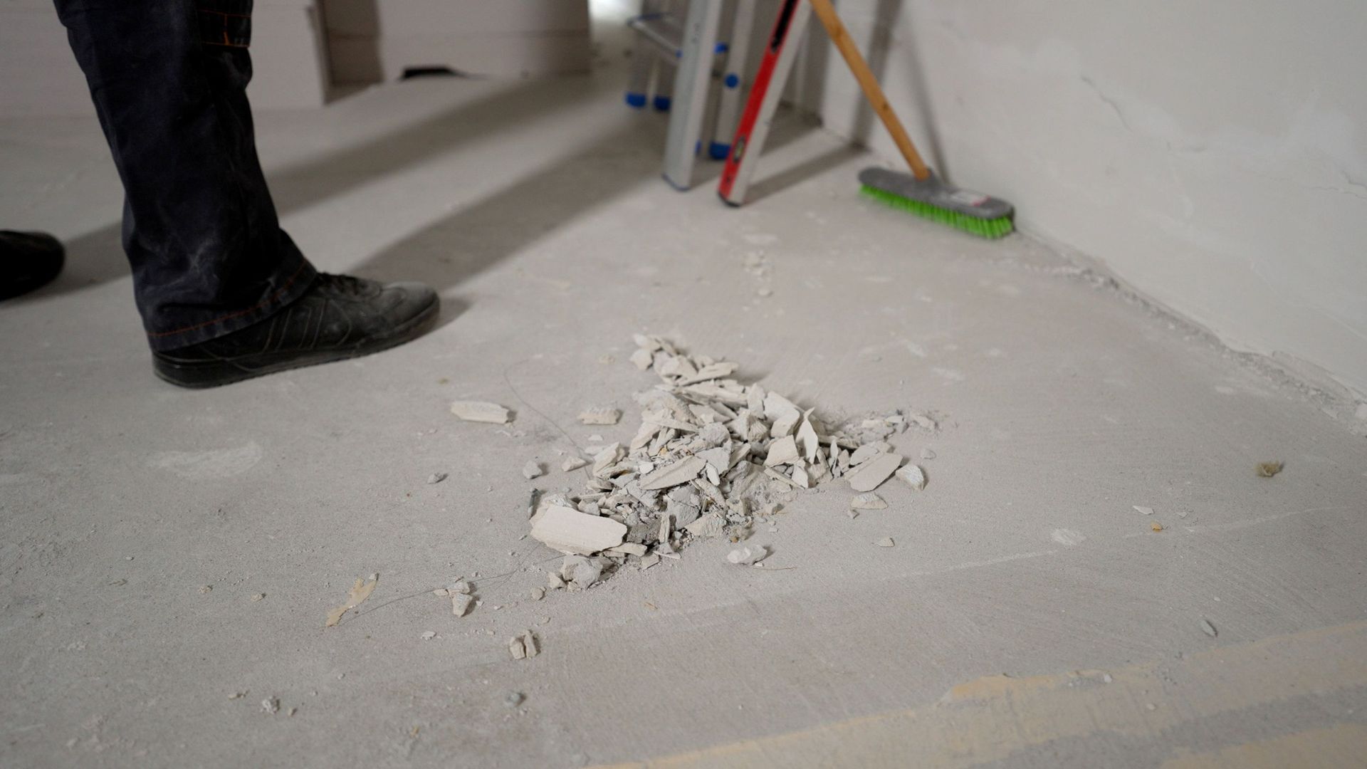 Person's feet near debris on a concrete floor in a room under construction.