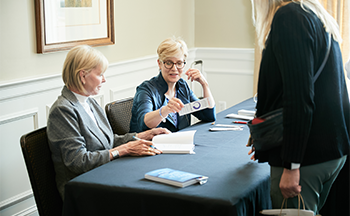 Three women are sitting at a table talking to each other.