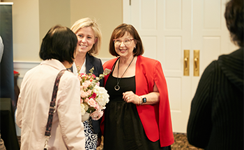 A woman in a red jacket is holding a bouquet of flowers and talking to another woman.