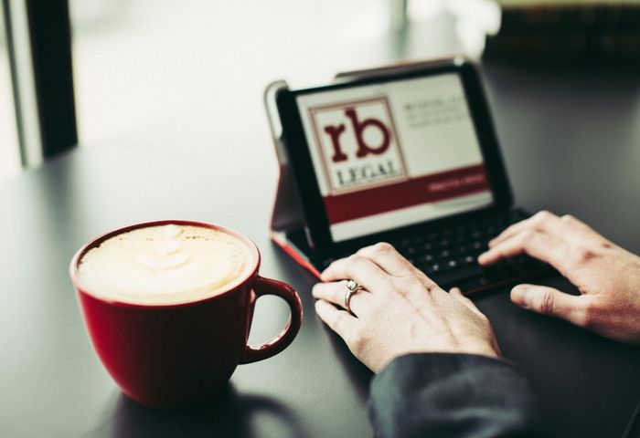 A person is typing on a tablet next to a cup of coffee