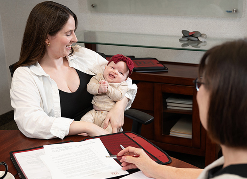 A woman is holding a baby while sitting at a desk.