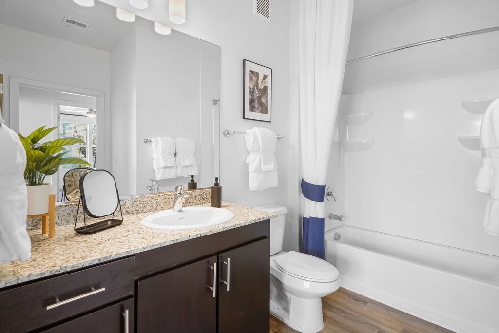 Modern apartment bathroom with granite countertop, dark wood vanity, and a tub/shower.